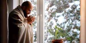 Homme qui a froid devant sa fenêtre